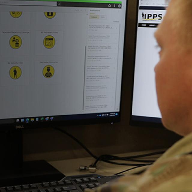 A person in military uniform views a computer screen displaying a grid of yellow icons with various symbols.