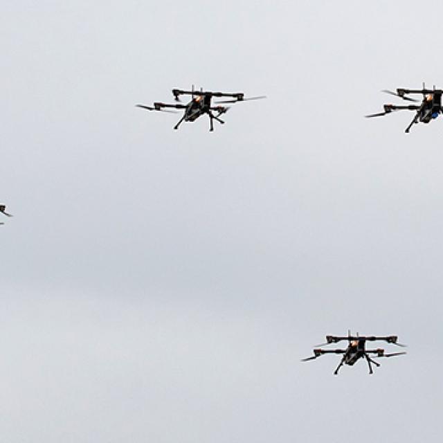 Four drones fly in formation against a cloudy sky, showcasing precision and technology.