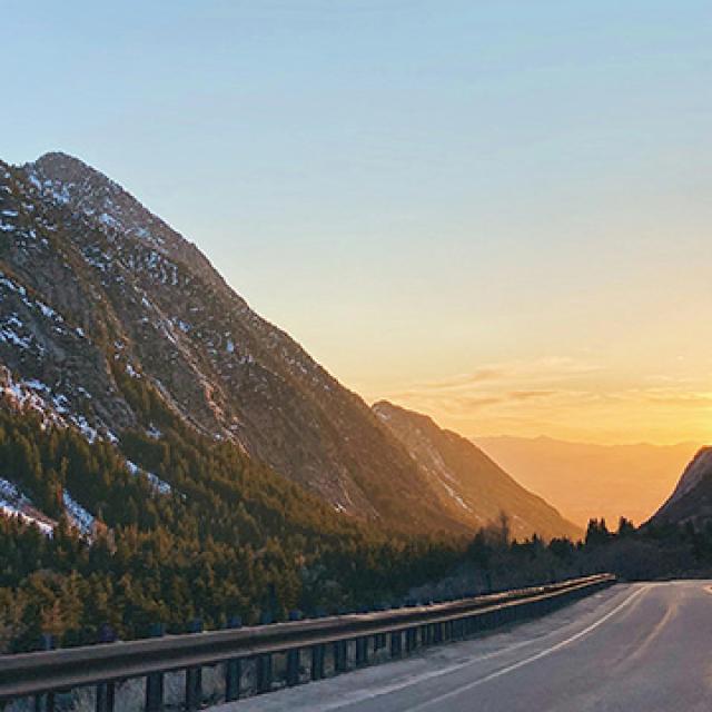 Mountain road curves through a serene valley at sunset.
