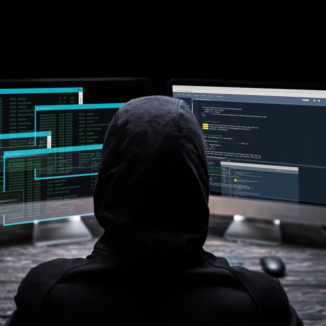 A person in a hoodie sits at a computer, focused on the screen, with a neutral background.