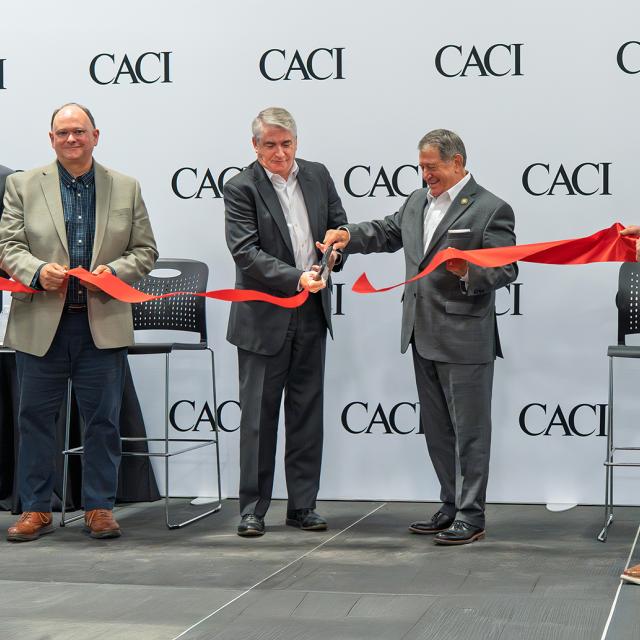 CACI's new facility opening in Rochester, showcasing a modern building with a large sign and attendees celebrating the event.