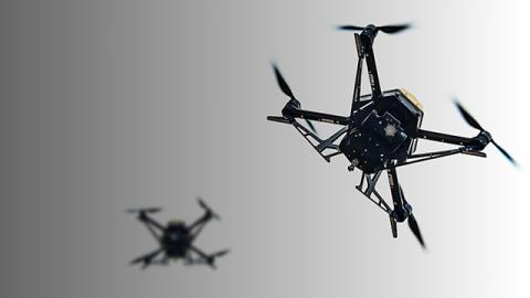 A close-up of a black drone with four spinning propellers in flight against a gradient background.