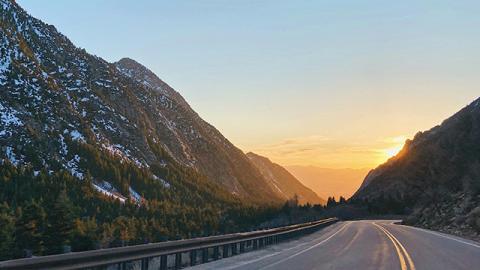 Mountain road curves through a serene valley at sunset.