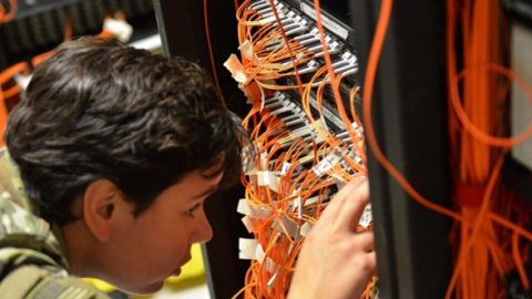A soldier is focused on organizing and managing a rack of cables in a technical environment.