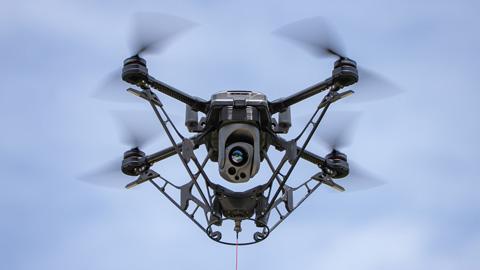 A small black drone is soaring through a clear blue sky.