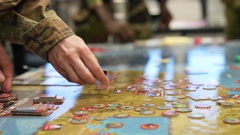 A soldier points to a detailed map spread out on a table, indicating a specific location or route.