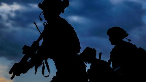 Silhouette of three soldiers standing resolutely against a dark, cloudy sky at dusk.