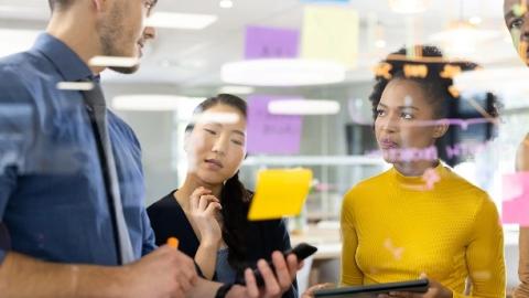 A diverse group of individuals collaborates around a table covered with colorful sticky notes, engaged in discussion.