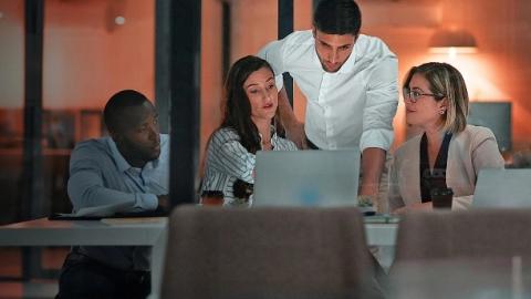 Three individuals focused on their laptops in a modern office environment, collaborating on a project.