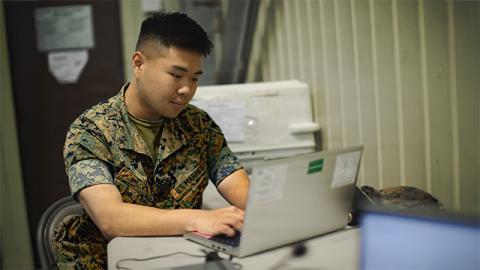 A man in military uniform seated at a desk, focused on paperwork in a professional office setting.