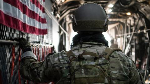 A soldier stands in the doorway of an airplane, ready to embark on a mission, with a focused expression.