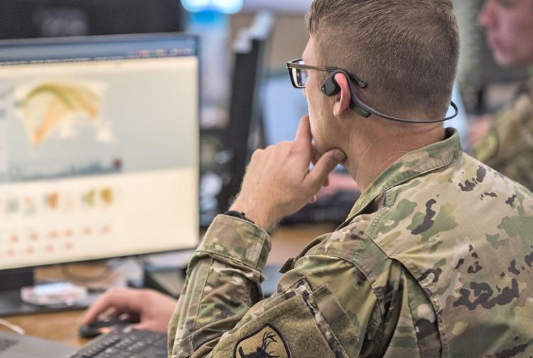 A soldier in uniform is focused on using a computer, showcasing technology in a military setting.