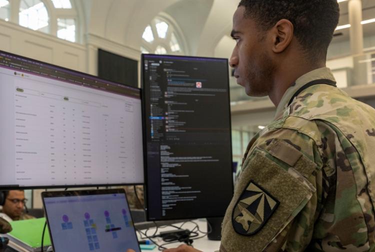 A soldier in uniform intently observes a computer screen, showcasing a moment of focus and dedication to duty.