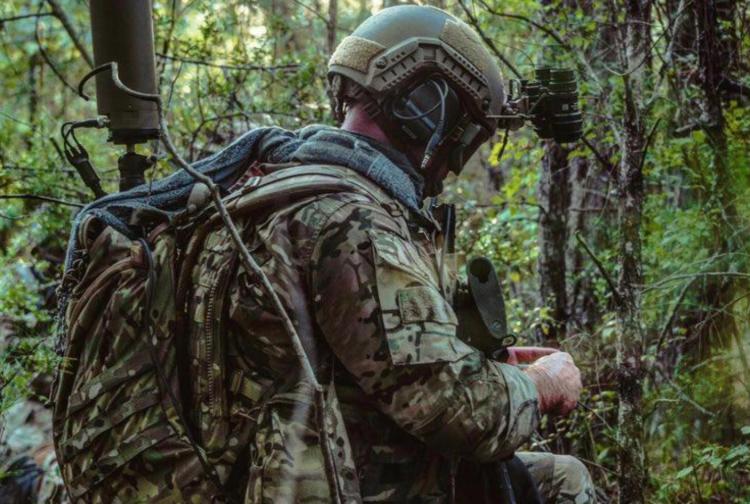 Two military personnel standing in front of a computer screen, engaged in discussion or analysis of information displayed.