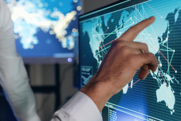 A man points at a computer screen displaying a detailed map, indicating a specific location or route.