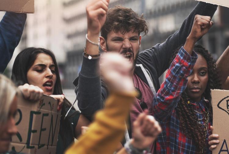A diverse group of people protesting, holding various signs with messages advocating for social change and justice.