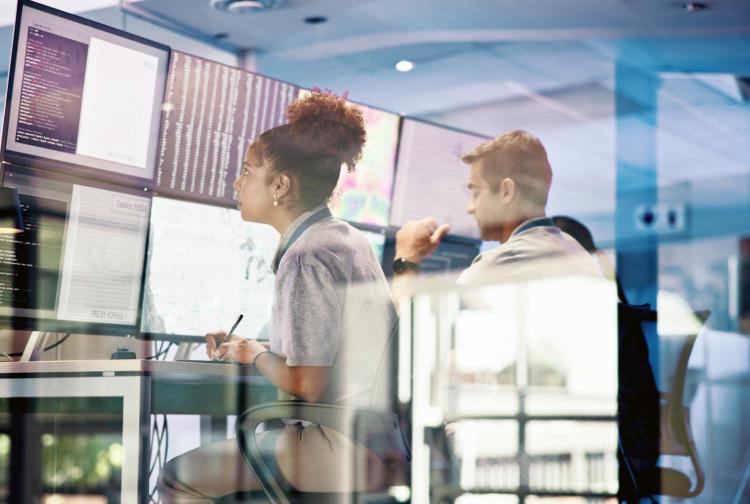 Two individuals focused on their computers while collaborating in a modern office environment.
