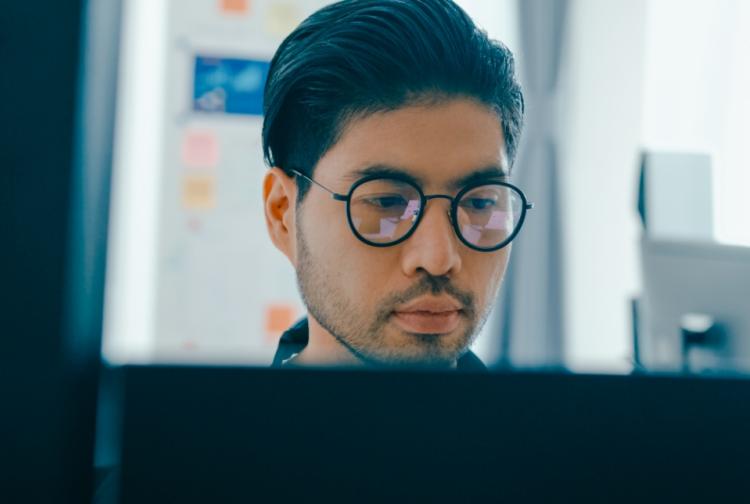 A man with glasses intently gazes at a computer screen, focused on his work or research.