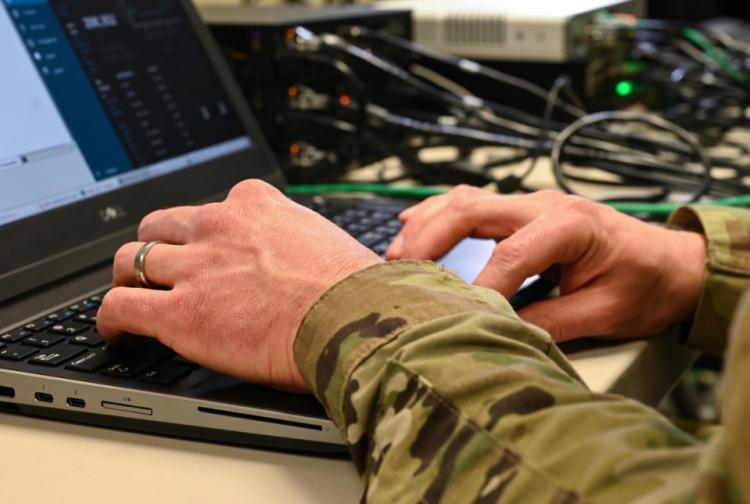 A soldier seated at a desk, focused on using a laptop computer in a military setting.