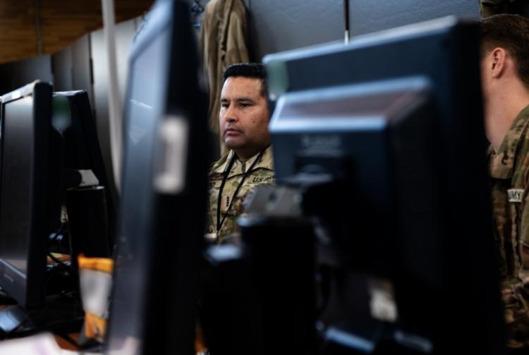A soldier intently examines a laptop computer while seated, focused on the screen's content.
